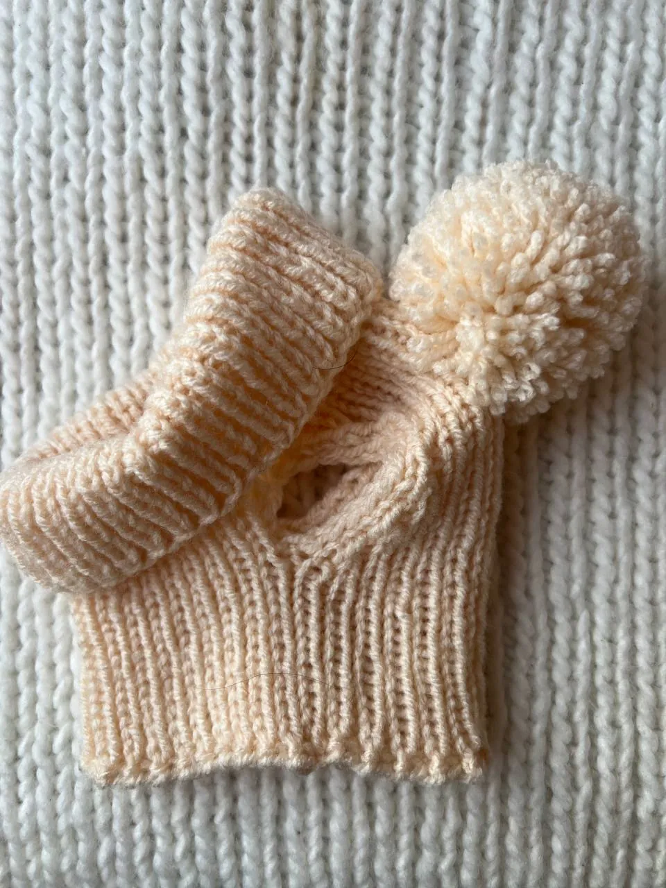 Beige knitted dog beanie with a cream pom-pom, laid flat